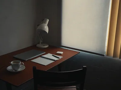 A small desk with a closed laptop, an open notebook, a pen and a cup of coffee