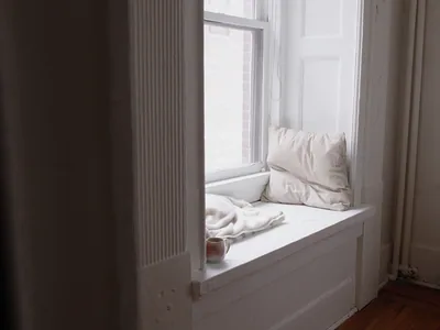 A window seat with a cushion, a folded blanket and one coffee cup in morning light