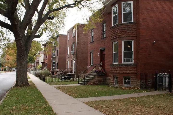 A quiet block of brick two flats with front stoops under autumn trees